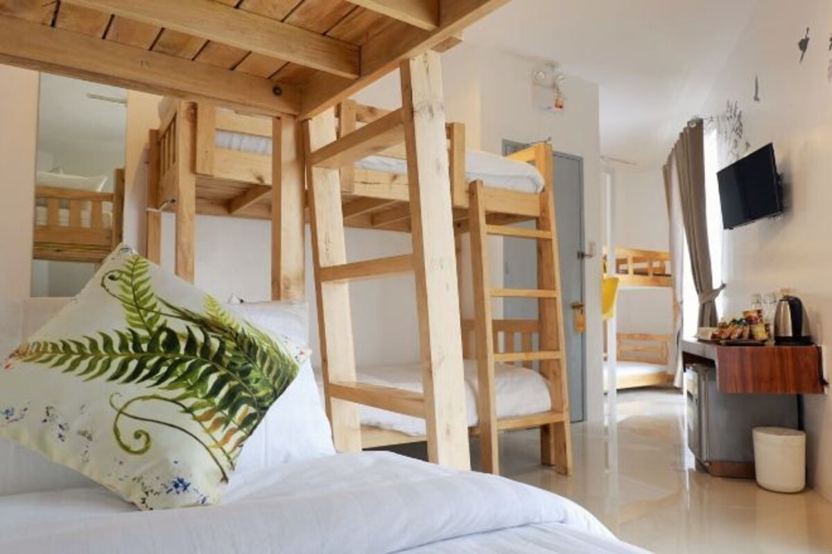 A room with bunk beds, a wooden ladder, a television, and a small kitchenette.