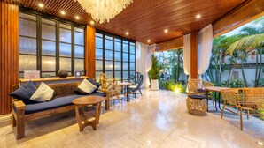 A spacious room with a wooden ceiling, large windows, and a view of palm trees. There is a sofa, a table, and wicker chairs. - The Akasha Seminyak Bali Boutique Hotel (Keroboken Kelod)