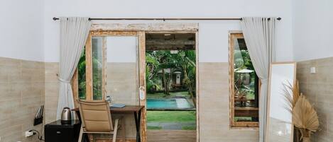A hotel room with a bed, a desk, and a view of a swimming pool and garden.