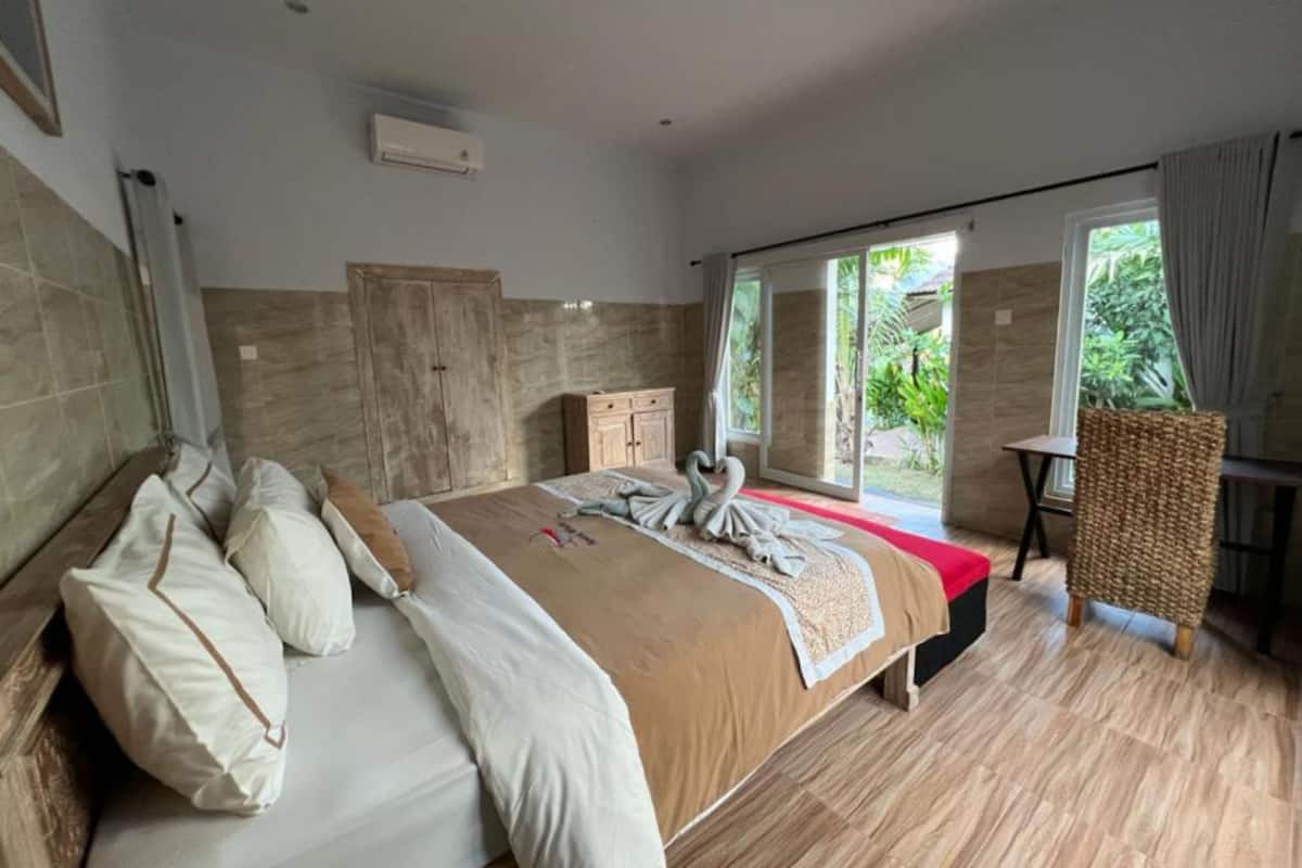 Ein Schlafzimmer mit einem großen Bett, einem Holzschrank, einem kleinen Tisch und Blick ins Grüne.