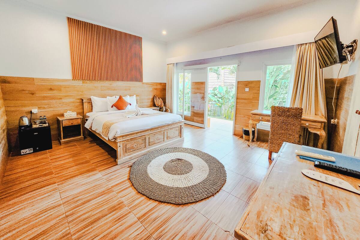 Ein geräumiges Schlafzimmer mit einem großen Bett, einem Holzkopfteil, einem Nachttisch, einem Schreibtisch, einem Stuhl und einem großen Fenster mit Blick auf Grünflächen.