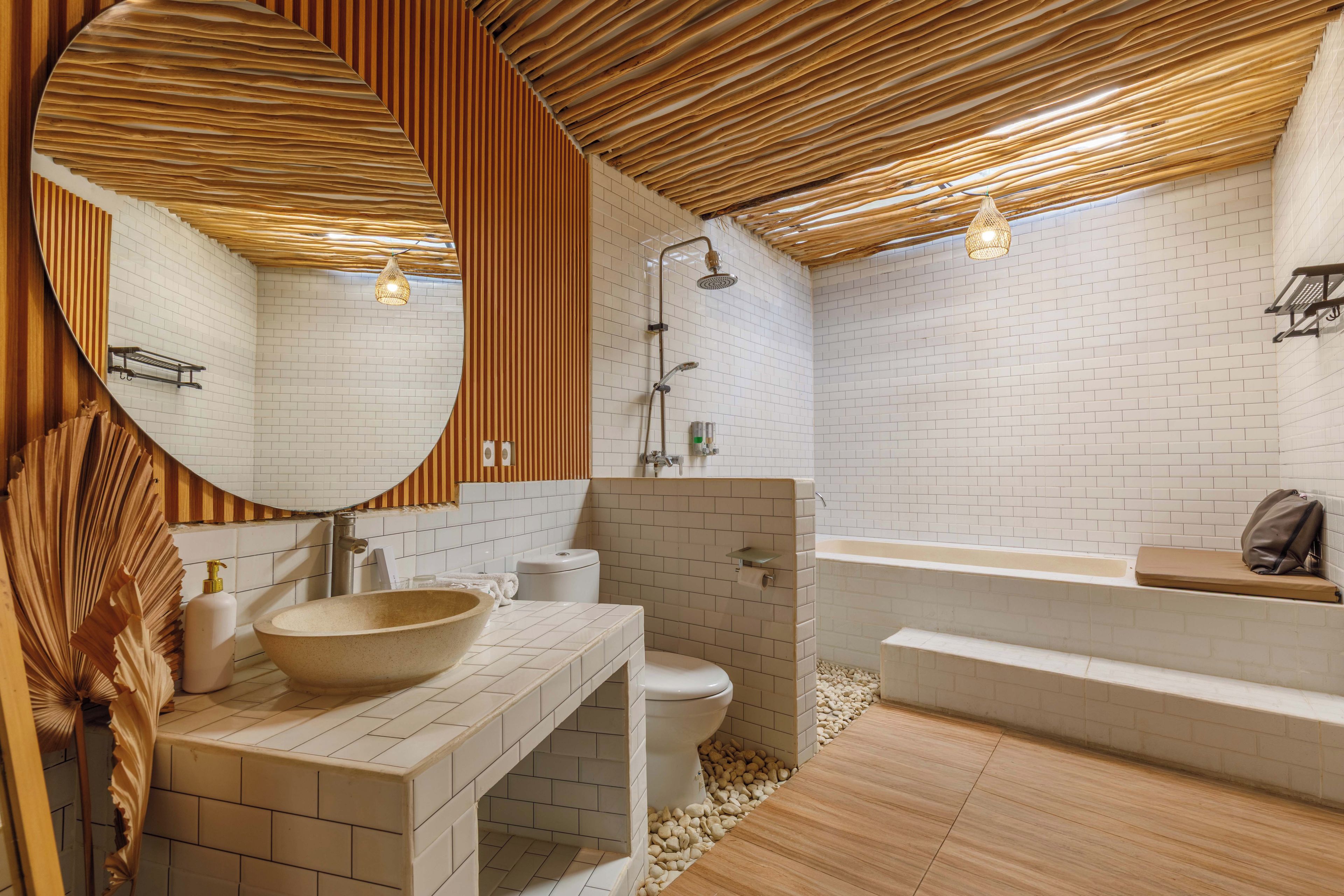 Un baño moderno con techo de madera, un espejo redondo grande, un lavabo sobre encimera, inodoro y bañera.