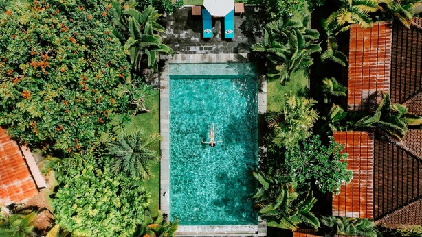 An aerial view of a rectangular swimming pool surrounded by lush greenery and a tiled roof. - Agung Wiwin Homestay (Munggu)