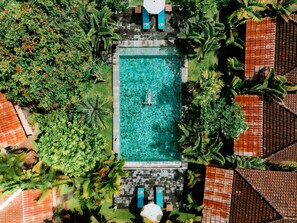 An aerial view of a rectangular swimming pool surrounded by lush greenery and a tiled roof. - Agung Wiwin Homestay (Munggu)