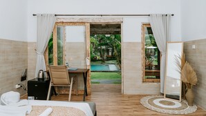 A hotel room with a bed, a desk, a chair, a small table with a kettle, and a view of a swimming pool and garden. - Agung Wiwin Homestay (Munggu)