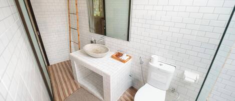 A bathroom with white tiled walls, a wooden floor, a white sink with a bowl, a toilet, and a glass shower enclosure.
