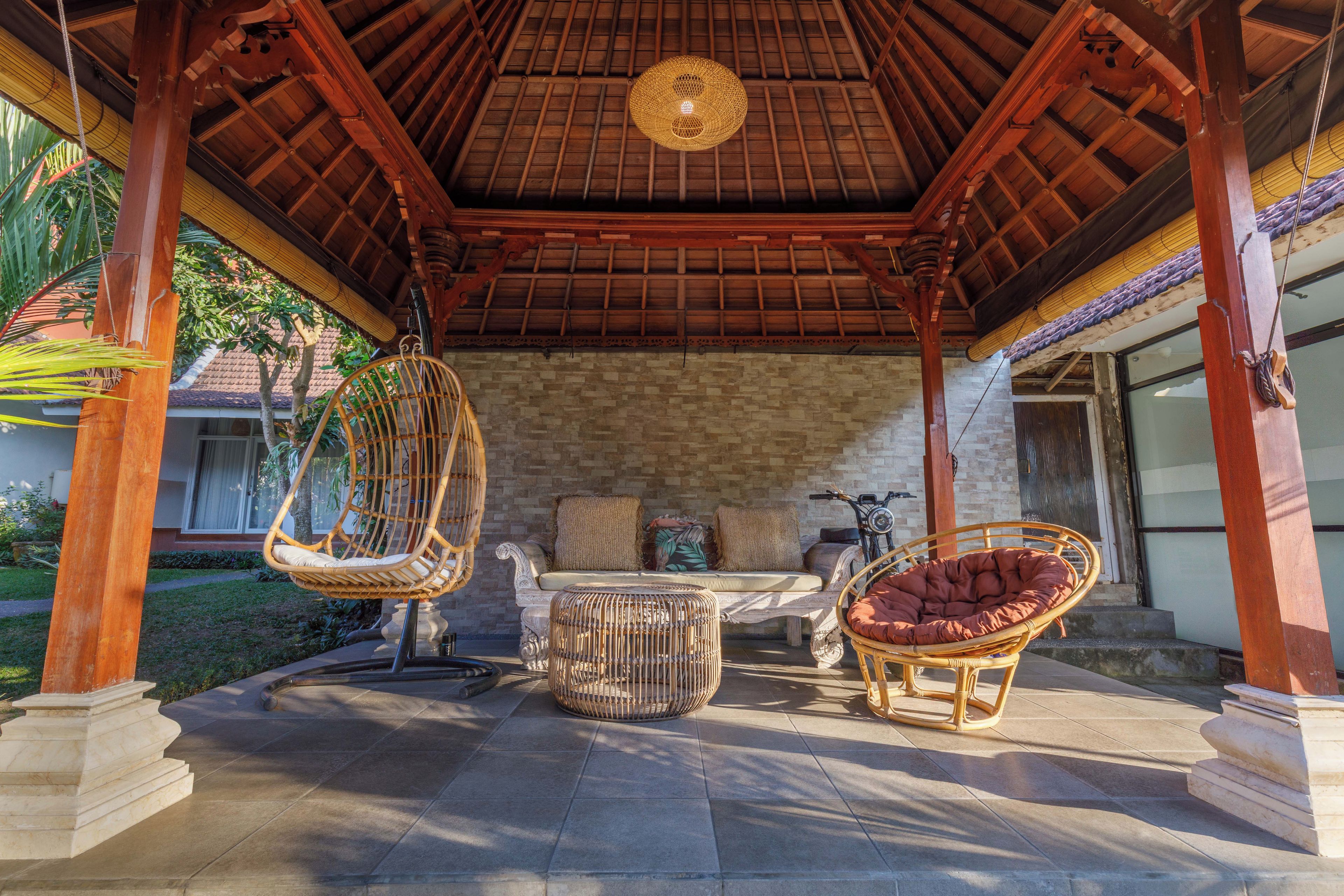 A covered outdoor seating area with wicker furniture and a stone wall backdrop.