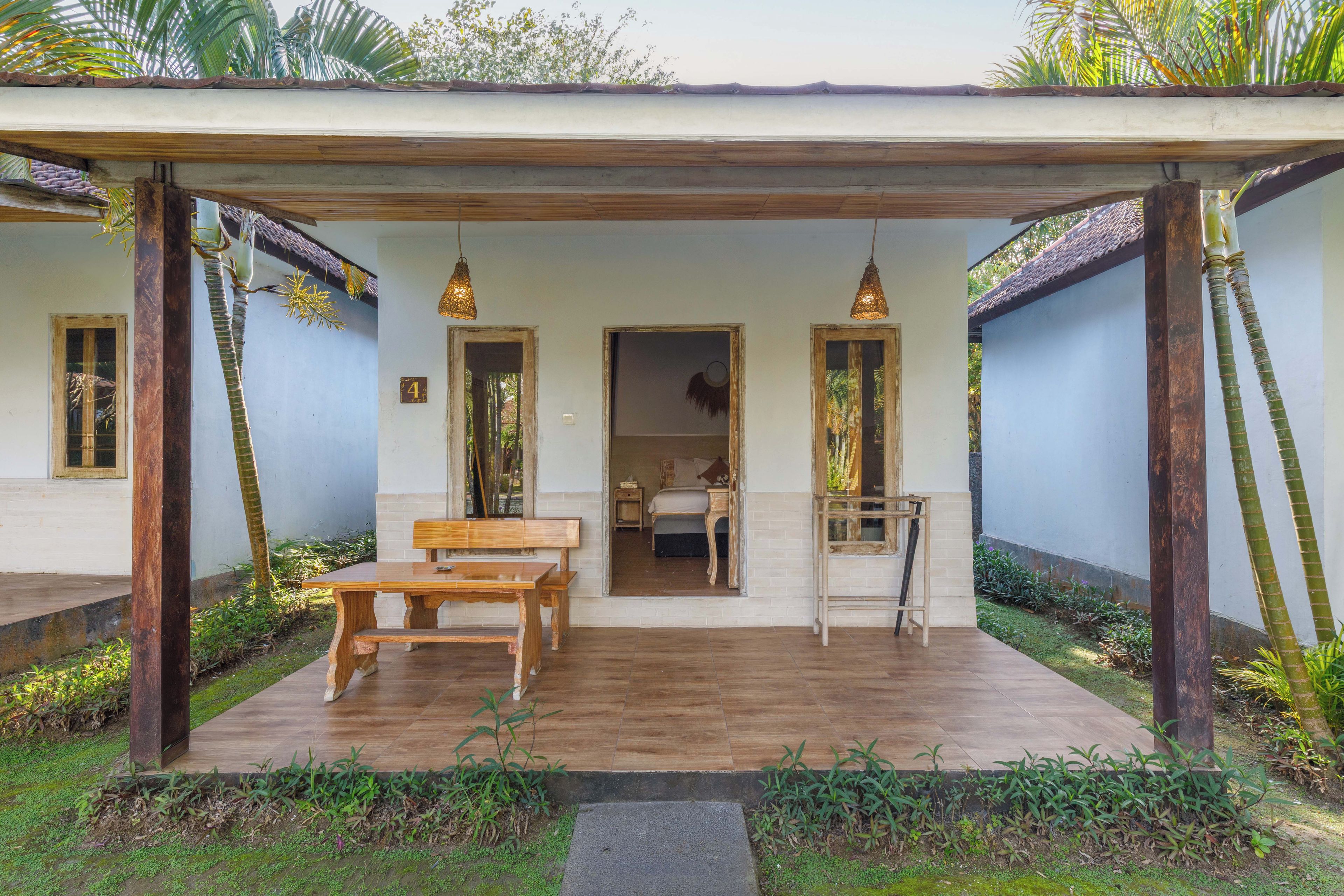 A covered outdoor seating area with a wooden table and benches, a small garden with plants, and a view of the interior through an open doorway.