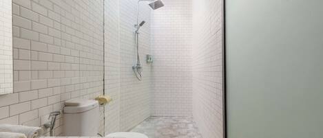 A bathroom with white tiled walls, a toilet, a shower, and a wooden floor.
