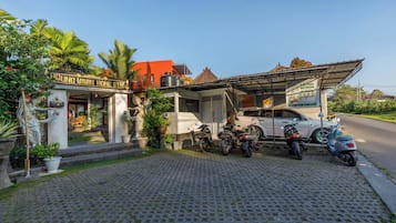 A building with a sign that reads 'GUNG WIWIN HOME STAY'. There are motorcycles parked in front, and a car is parked on the side.