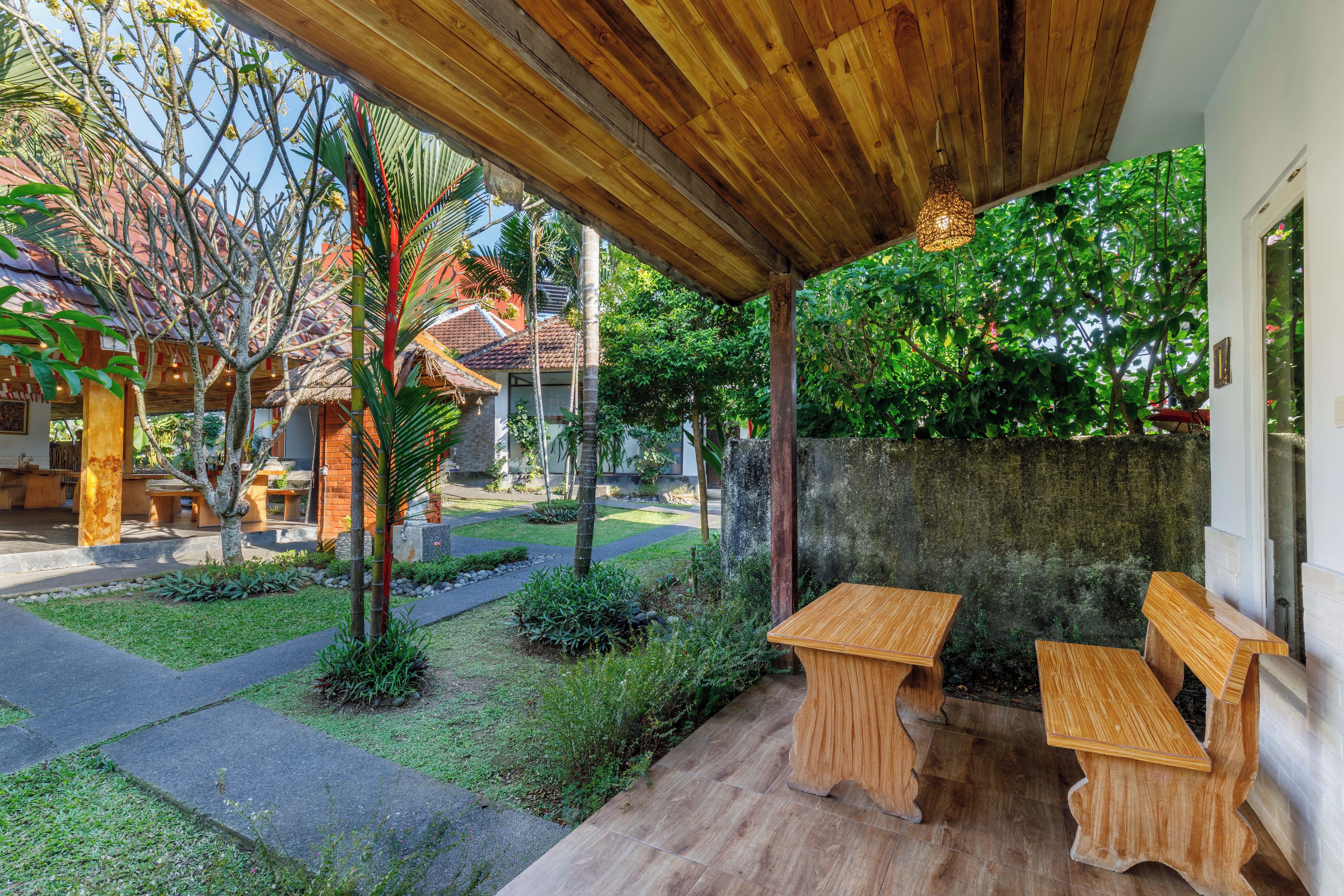 A covered outdoor seating area with wooden furniture, a stone wall, and a garden with various plants.