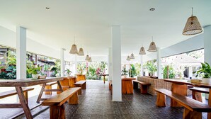An indoor dining area with wooden benches and tables, stone flooring, and hanging wicker lamps. - Agung Wiwin Homestay (Munggu)