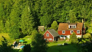 Una casa rossa con tetto spiovente, immersa in una rigogliosa foresta verde.