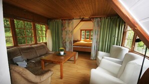 Una stanza accogliente con soffitto in legno, un letto, un divano, una poltrona e un tavolo con una pianta.