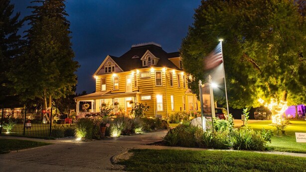 A large, yellow wooden house with a dark roof, surrounded by greenery and a paved driveway. - Lavender Fields Inn B&B (Calmar)