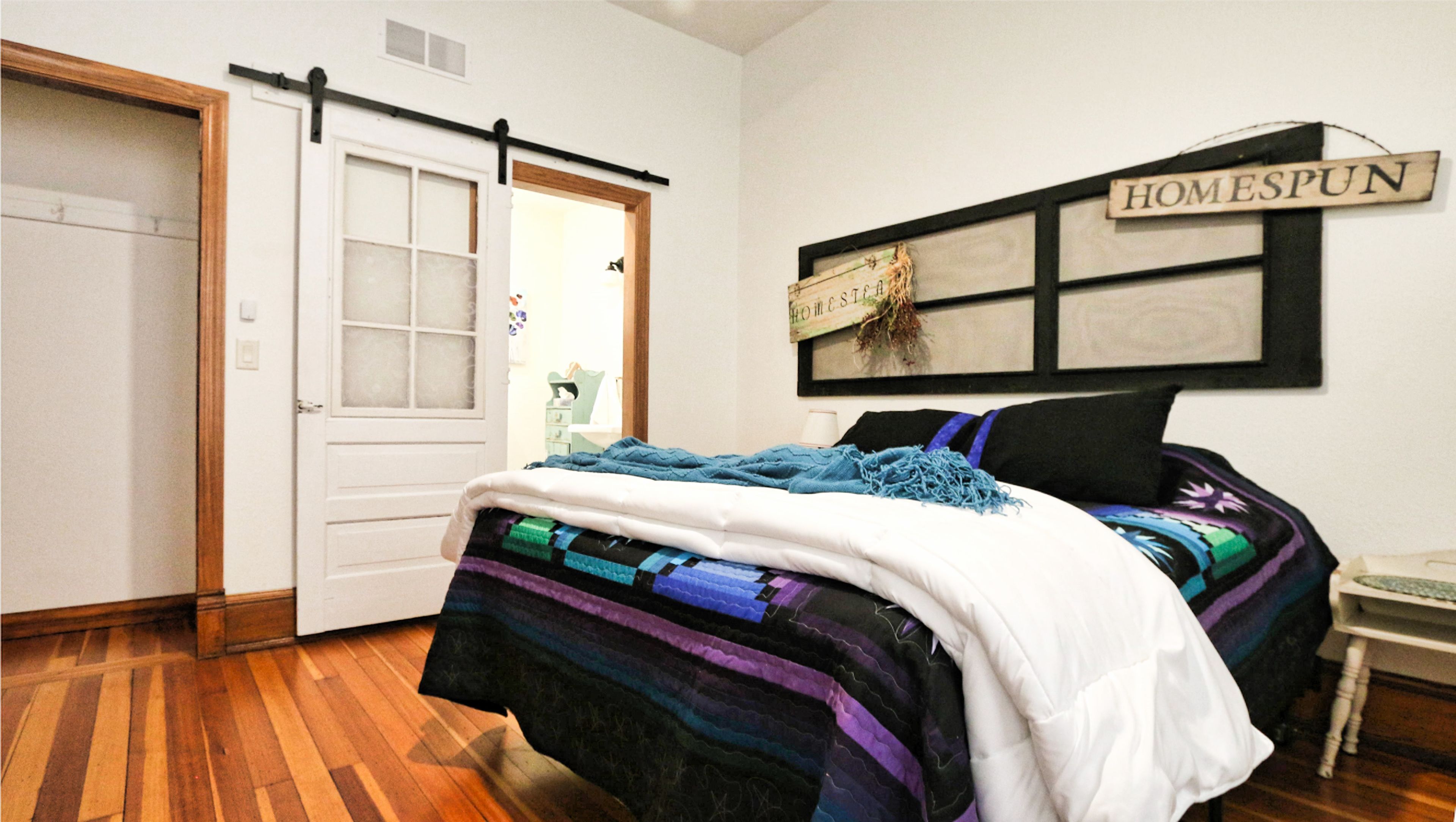 A bedroom with a bed, a door, a wall-mounted sign, and a small table.