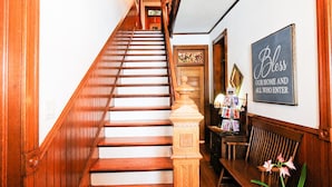 A wooden staircase with a handrail, a bench, and a wall sign that reads "Bless our home and all who enter." - Lavender Fields Inn B&B (Calmar)