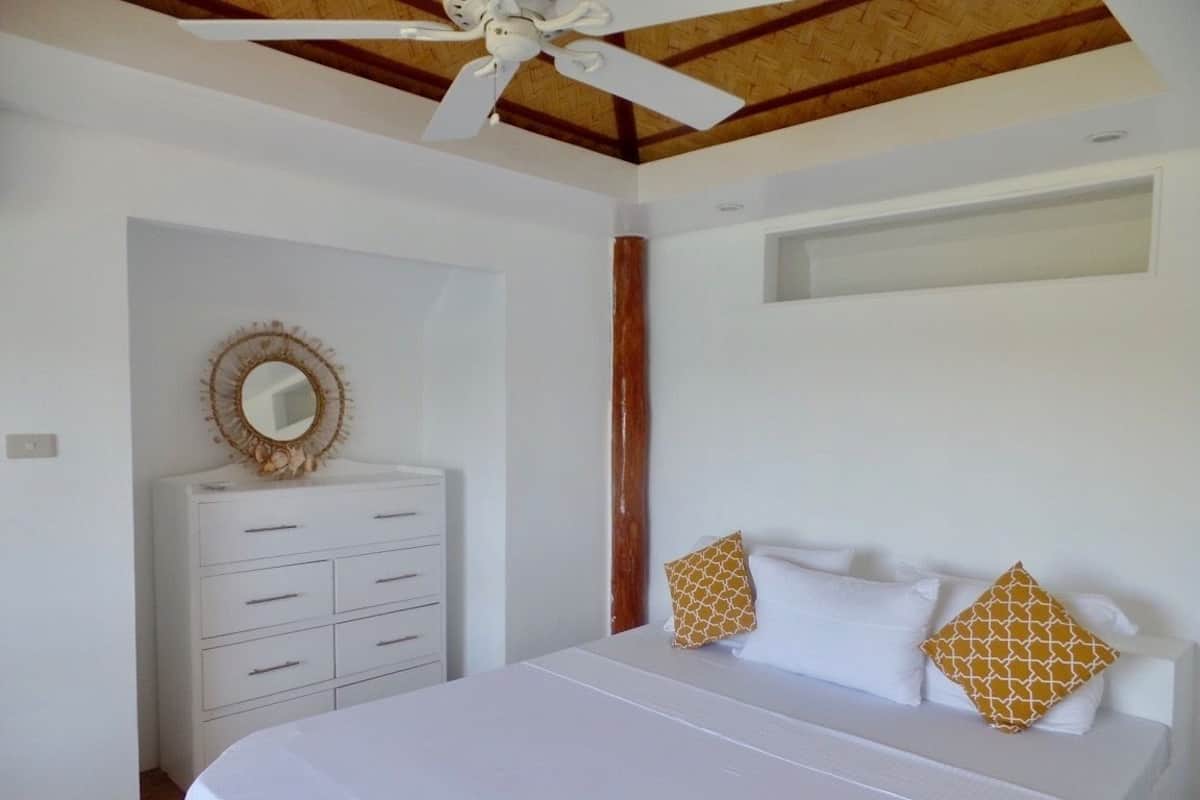 Ein Schlafzimmer mit einem Bett, einem Deckenventilator, einem Schminktisch und einem Spiegel.