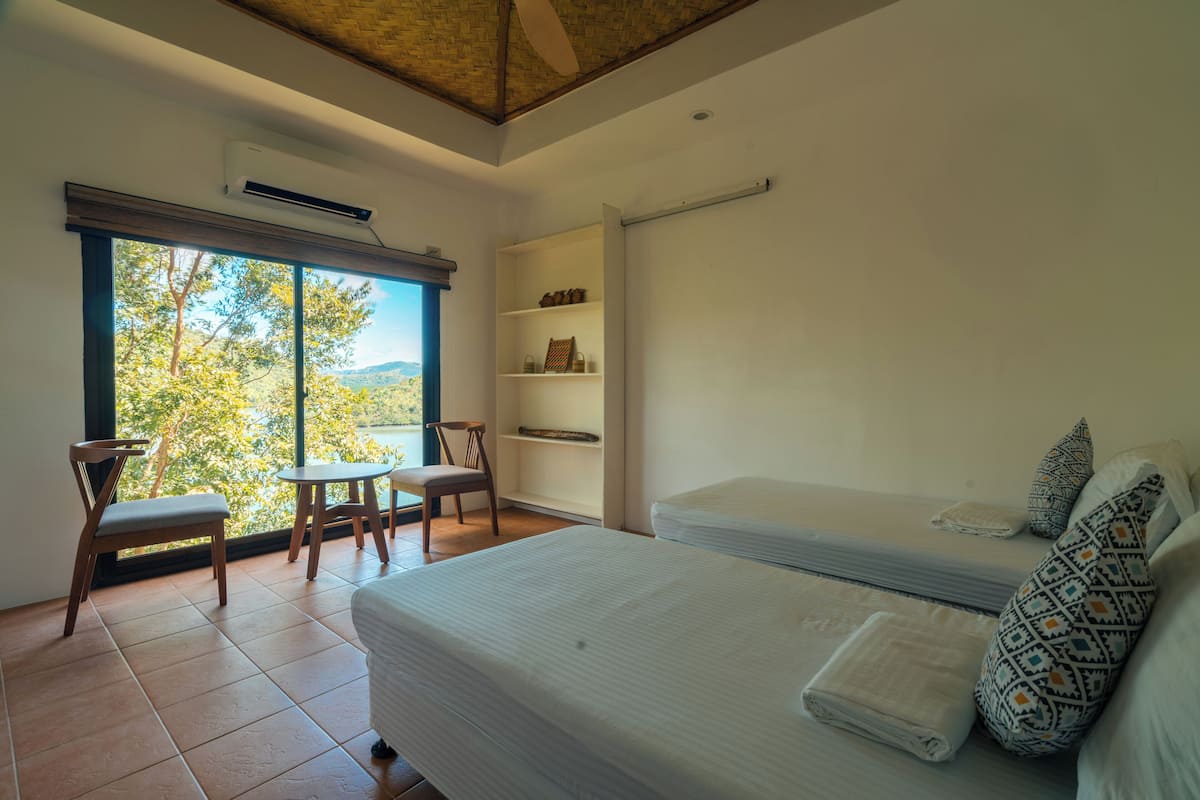 Ein Schlafzimmer mit großem Fenster, einem Bett, einem Sessel, einem kleinen Tisch und einem Regal mit Dekoration.