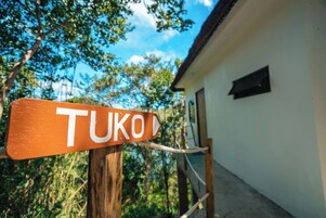 Un letrero de madera con la palabra 'TUKO' que señala hacia la derecha, frente a un edificio de fachada blanca y una ventana.