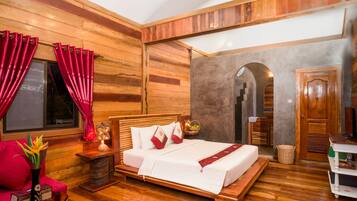 A wooden-paneled room with a bed, red curtains, a small table with a vase, and a wooden bench.