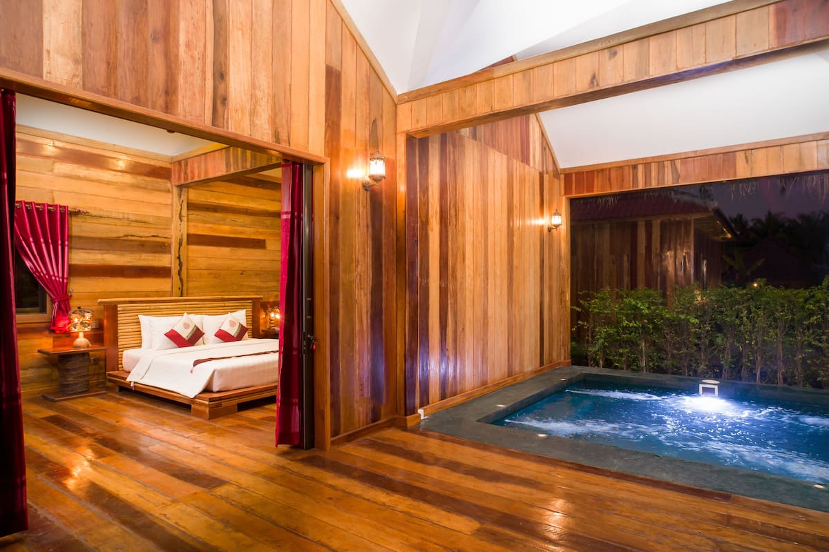 A wooden interior with a bed, a hot tub, and a view of greenery outside.