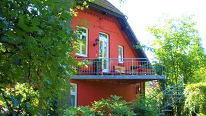 Ein rotes Gebäude mit einem Balkon, umgeben von üppigem Grün.