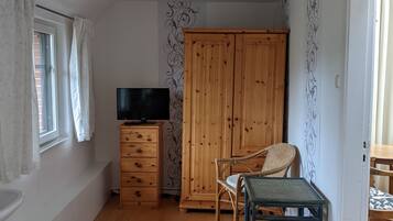 Een slaapkamer met een bed, een houten garderobe, een televisie op een dressoir, een raam met gordijnen en een kamer met een patroon op de muur.