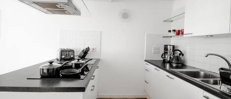 Una cocina moderna con armarios blancos, encimera negra y una campana extractora de acero inoxidable.
