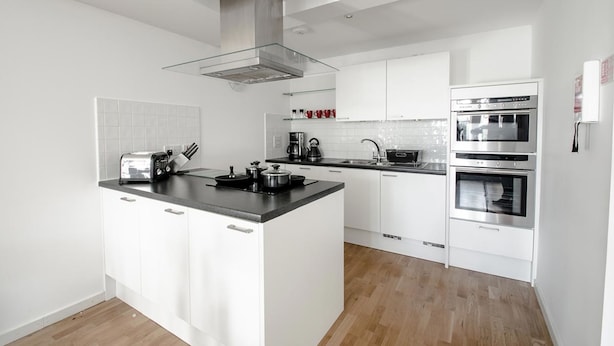 Een moderne keuken met witte kasten, een centraal eiland met een kookplaat, twee ovens en een glazen afzuigkap.
