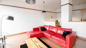 A modern living room with a red leather sofa, a wooden coffee table, and a black floor lamp. - Orange Apartments - 13 Bastille (Aberdeen)