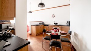 A modern kitchen with wooden cabinets, a dining area with a table and chairs, and pendant lighting. - Orange Apartments - 13 Bastille (Aberdeen)