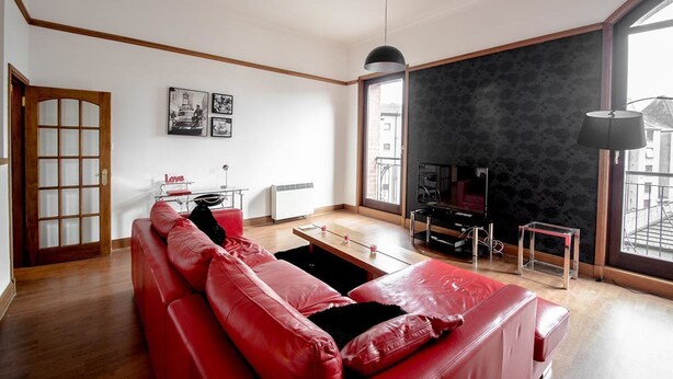 A living room with a red leather sofa, a small wooden table, and a black lamp. - Orange Apartments - 13 Bastille (Aberdeen)