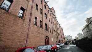 A red brick building with multiple windows and a narrow alleyway with parked cars. - Orange Apartments - 13 Bastille (Aberdeen)