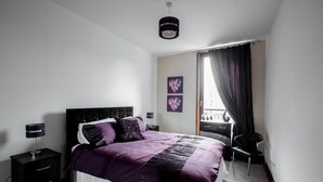 A modern bedroom with a large bed, bedside tables, a desk, and a chair. - Orange Apartments - 13 Bastille (Aberdeen)