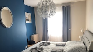 Un dormitorio con una cama, un espejo redondo, un radiador, una ventana con cortinas y una lámpara colgante.