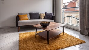 A modern living room with a sofa, a coffee table, and a large window with a view of buildings. - The apartment of Stanislas (Nancy)