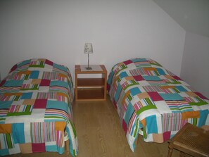 Quarto pequeno com duas camas de solteiro, uma mesinha de cabeceira e uma cadeira.