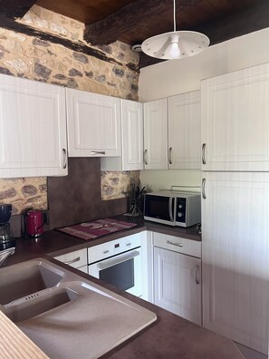 Una cocina con armarios blancos, microondas, tetera y fregadero.
