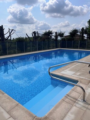 Una piscina rectangular con borde de azulejos, rodeada por una valla, y un cielo despejado arriba.