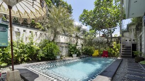A swimming pool with a checkered tile border, surrounded by greenery and a building with a dome structure. - Hotel O Anika Guest House (Tuban)