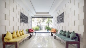 A modern lobby with two wooden benches, each with cushions, flanking a central walkway. - Hotel O Anika Guest House (Tuban)