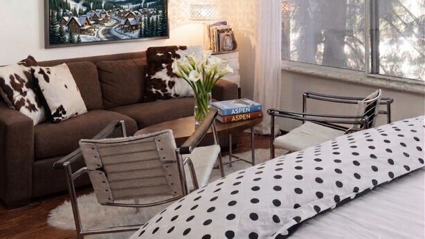 Ein gemütliches Zimmer mit einer Couch, einem kleinen Tisch mit Büchern, einem Sessel und einem Bett mit Punktenmuster-Bettwäsche.