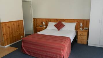 A hotel room with a wooden headboard, a single bed with a red blanket, two bedside tables with lamps, and a wardrobe.