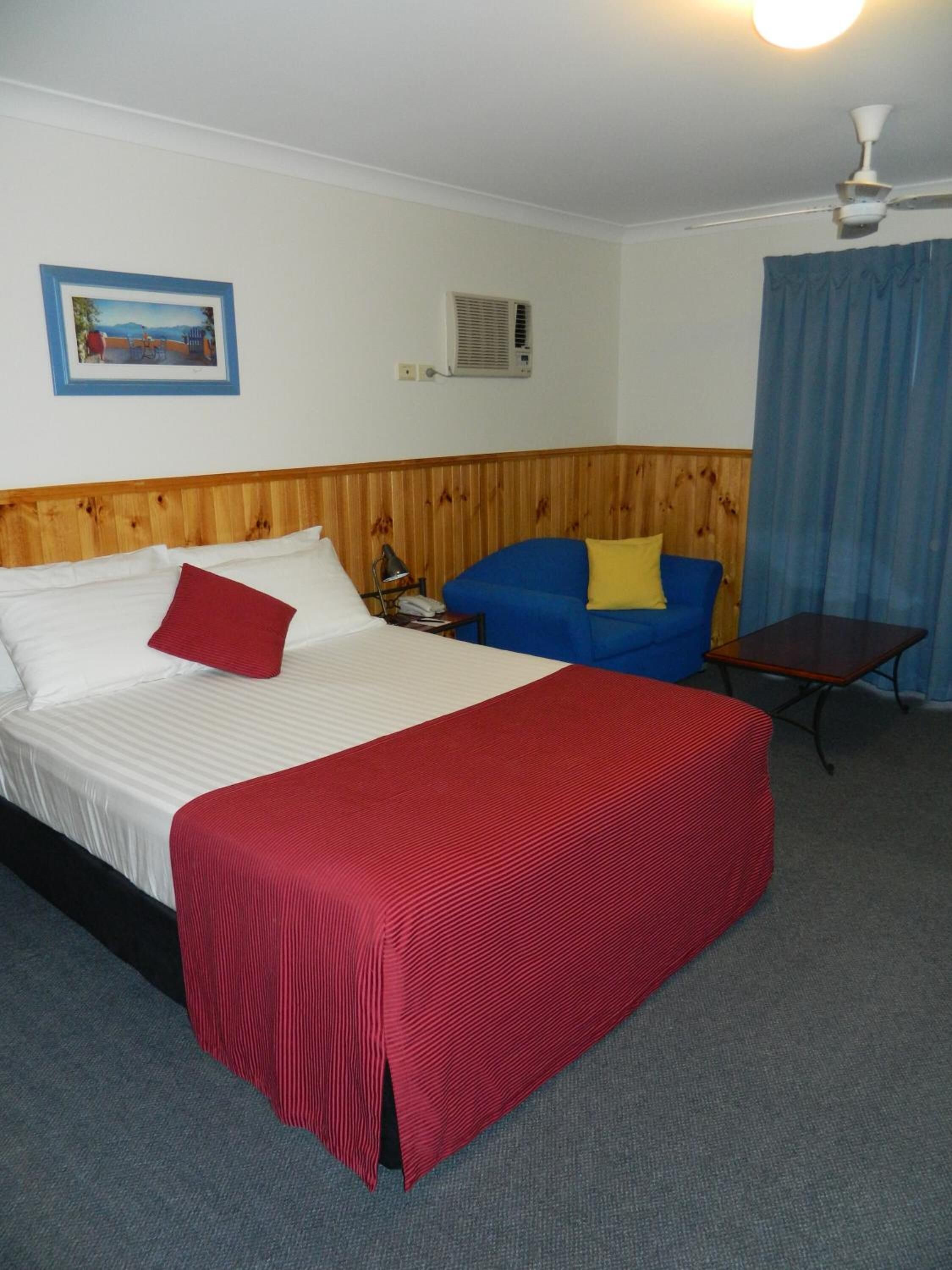 Quarto de hotel com cama, sofá azul, mesa pequena, ventilador de teto e um quadro na parede.