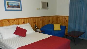 A hotel room with a bed, a blue sofa, a small table, a ceiling fan, and a picture on the wall.