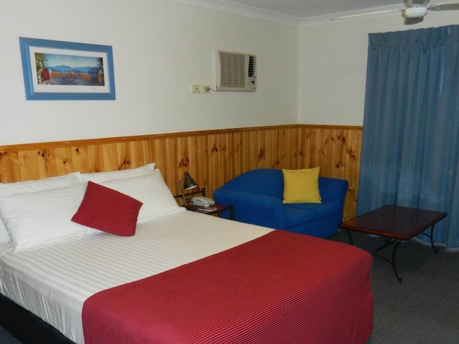 A hotel room with a bed, a blue sofa, a small table, a ceiling fan, and a picture on the wall.