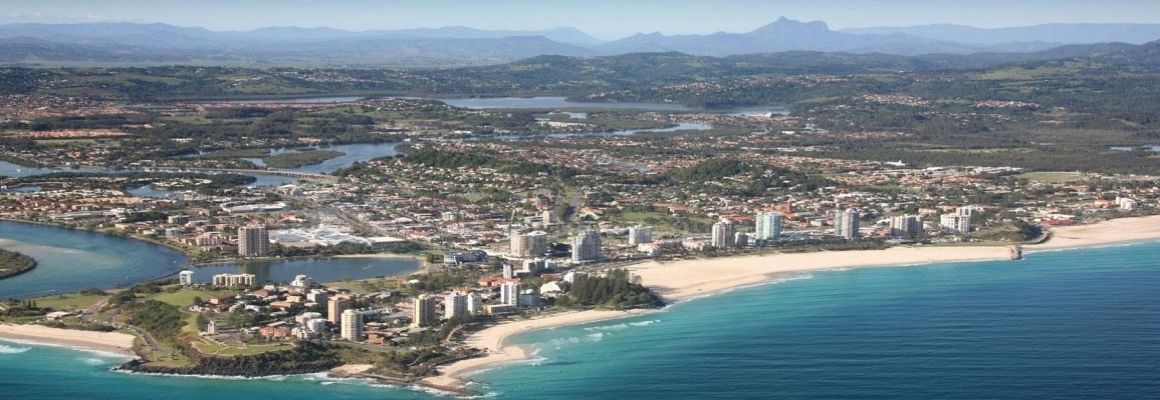 Vista aérea de una ciudad costera con playa, cuerpos de agua y una zona urbana densa.