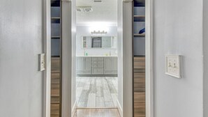 A hallway leading to a bathroom with a vanity, mirror, and light fixtures.