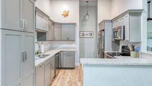 A modern kitchen with grey cabinets, stainless steel appliances, a granite countertop, and a wooden floor.